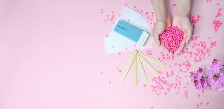 Set of depilation and beauty on pink background concept - sugar paste or hair removal waxing melted paste and stripes, orchid and female hands. Film Wax Granules or hot wax, cartridge, wooden spatulaの写真素材