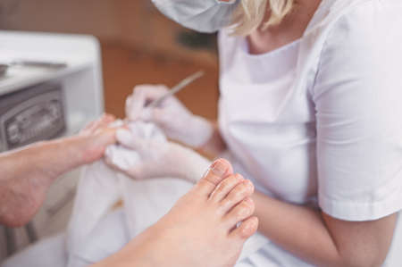 Professional medical pedicure procedure close up using double nail instrument. Patient visiting chiropodist podiatrist. Foot treatment in SPA salon. Podiatry clinic. Pedicurist hands in white glovesの写真素材