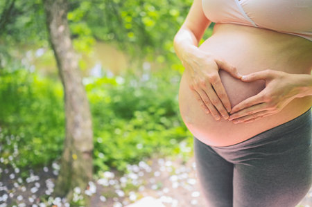 Beautiful young pregnant woman doing yoga exercising in park outdoor. Sitting and relaxing on pink...