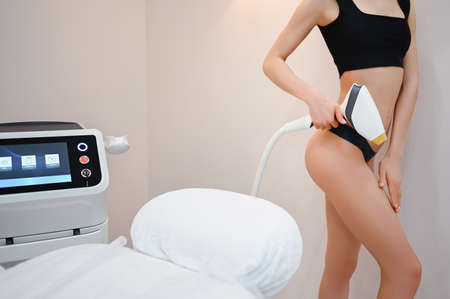 Beautiful fit womans body with smooth soft skin in black lingerie with laser apparatus device isolated in beauty salon.の写真素材