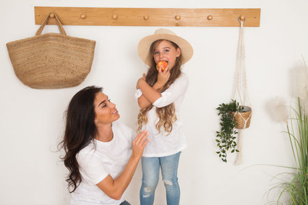 Mother puts on her little daughter a straw hat sitting on a bench in the Scandinavian style...