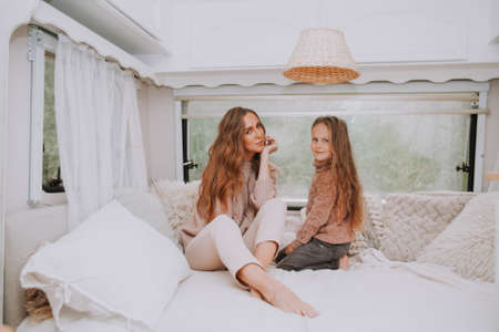 Happy family - mother and little daughter relaxing hugging and having fun in countryside inside white scandinavian rustic camper van interior. Domestic tourism conceptの写真素材