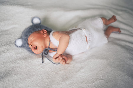 Cute crying newborn little baby boy sleeping in crib in a knitted suit with ears. Baby goods...