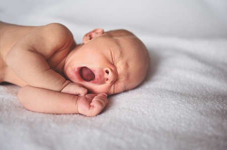 Cute emotional funny yawning newborn little baby boy sleeping in crib. Baby goods packaging template. Healthy child, concept of hospital and happy motherhood. Infant baby. Nursery.の写真素材