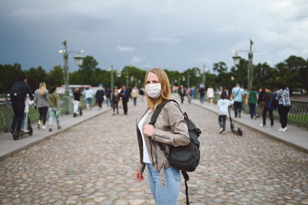 Young blonde woman walking in city street wearing face protective mask for Covid 19 prevention....
