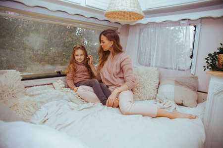 Happy family - mother and little daughter relaxing hugging and having fun in countryside inside white scandinavian rustic camper van interior. Domestic tourism conceptの写真素材