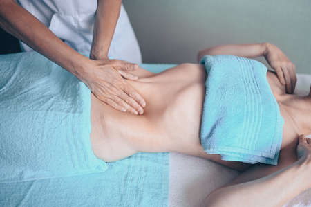Young unrecognizable woman lying on massage table and enjoying therapeutic massage. Body care, losing weight concept. Hands masseur massage therapist doing anti-cellulite massage in spa clinicの写真素材