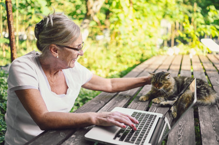 Technology, old age people concept - elderly happy senior woman with home cat working online with...