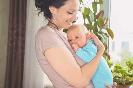 Beautiful mother holding in arms her little cute newborn infant son. Baby facial expressions. Family at home by the window. Healthy child, concept of hospital and happy motherhood. Nursery.の写真素材