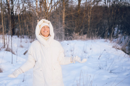 Happy elderly senior mature woman in white warm outwear playing with snow in sunny winter outdoors. Retired healthy people holiday vacation winter activities, active lifestyle conceptの写真素材