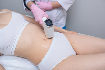 Laser epilation and cosmetology in beauty salon. Hair removal procedure. Laser epilation, cosmetology, spa, and hair removal concept. Beautiful blonde woman getting hair removing on stomachの写真素材