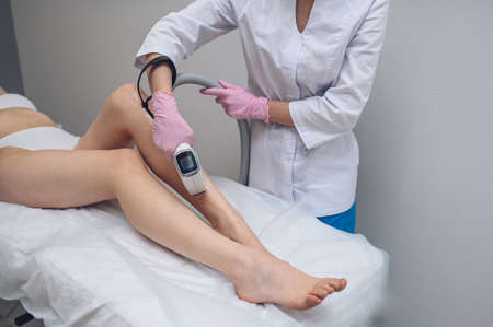 Laser epilation and cosmetology in beauty salon. Hair removal procedure. Laser epilation, cosmetology, spa, and hair removal concept. Beautiful blonde woman getting hair removing on legsの写真素材
