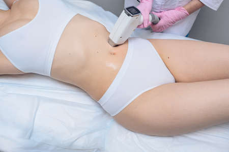 Laser epilation and cosmetology in beauty salon. Hair removal procedure. Laser epilation, cosmetology, spa, and hair removal concept. Beautiful blonde woman getting hair removing on stomachの写真素材