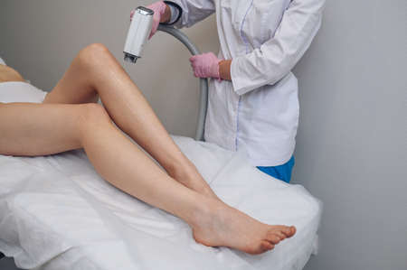 Laser epilation and cosmetology in beauty salon. Hair removal procedure. Laser epilation, cosmetology, spa, and hair removal concept. Beautiful blonde woman getting hair removing on legsの写真素材