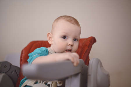 Little emotional newborn funny toddler boy sitting on feeding high chair. Baby facial expressions and goods packaging template. Healthy child, concept of hospital and happy motherhood. Infant babyの写真素材