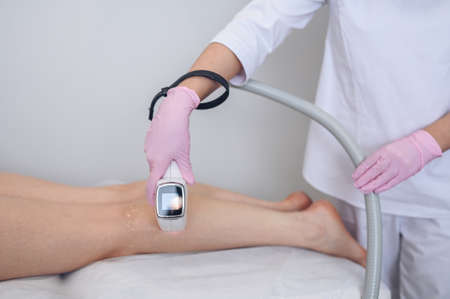 Laser epilation and cosmetology in beauty salon. Hair removal procedure. Laser epilation, cosmetology, spa, and hair removal concept. Beautiful blonde woman getting hair removing on legsの写真素材