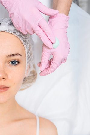 Beautiful happy woman receiving spa treatment. Cosmetologist in beauty salon with a pink glove...