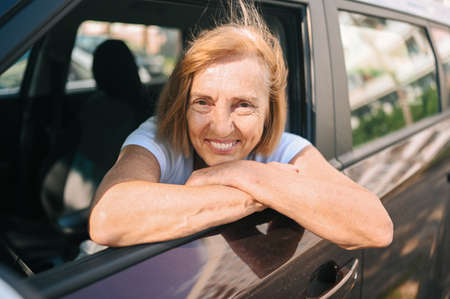 Happy senior woman driving sitting in new brown car, smiling looking at camera enjoying journey.Driving courses and life insurance concept. Retired people activity conceptの写真素材