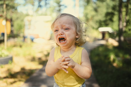 Close up portrait of little funny cute blonde girl child toddler in yellow bodysuit crying outside...