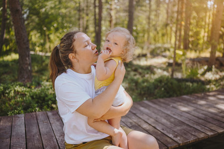 Little cute baby toddler girl blonde with curls on mothers arms. Mother and daughter playing spend...