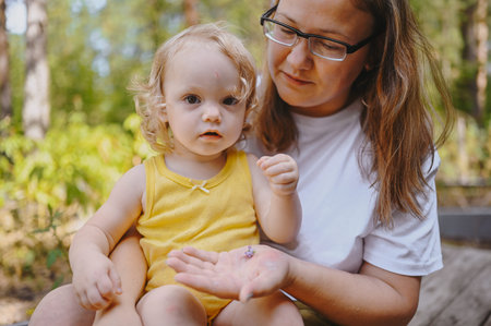 Little cute baby toddler girl blonde with curls on mothers arms. Mother and daughter playing spend...