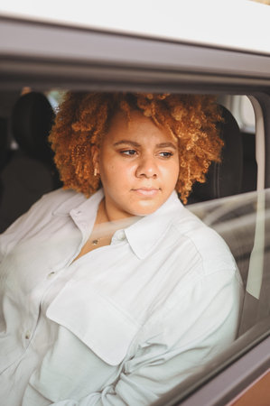 Happy young smiling African American woman red afro haired driver sitting in new brown car, smiling...