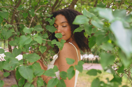 Fashion close up portrait of sensual attractive young naturally beautiful African American woman with afro hair posing in nature parkland in green foliageの写真素材