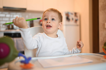 Little cute baby toddler boy blonde sitting on baby chair learning draw with colour pencils. Baby...