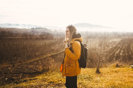 Young happy backpacker woman tourist traveling alone and posing at dawn with fog on background of...