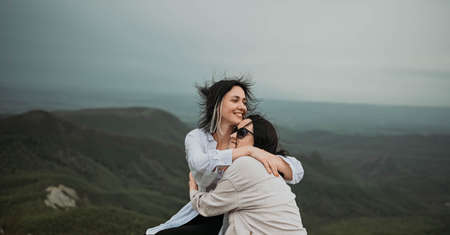 Young beautiful happy lesbian couple posing hugging in cloudy mountains outside at nature summer park. LGBT community concept. Female friends smiling enjoying moments together.の写真素材