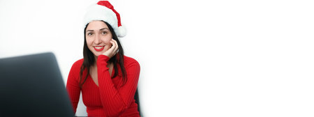 Beautiful smiling brunette woman in New Years Santa Claus hat works with laptop. Christmas and New...