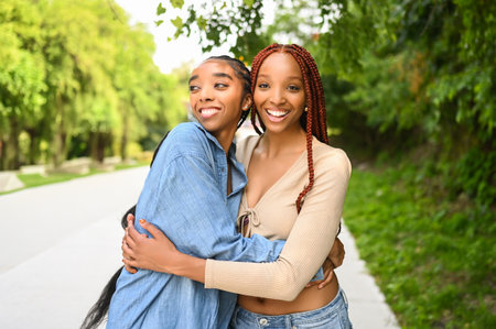 Street style portrait beautiful young African American female black couple. Braids hair, perfect white teeth smiling, sisters friends hugging walking outdoor in sunny summer day. Green park and cityの写真素材