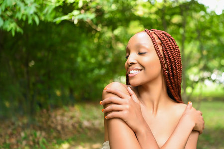 Close up portrait Beautiful young African American woman with red braids hair, perfect white teeth smiling outside, sunny summer day green foliage. Facial treatment. Cosmetology, skin care and spaの写真素材