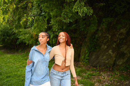 Street style portrait beautiful young African American female black couple. Braids hair, perfect white teeth smiling, sisters friends hugging walking outdoor in sunny summer day. Green park and cityの写真素材