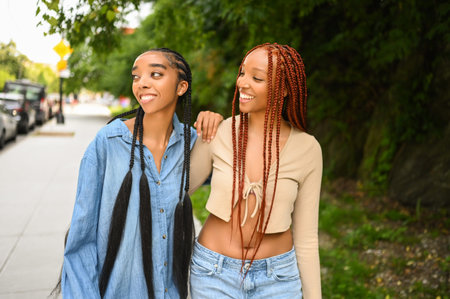 Street style portrait beautiful young African American female black couple. Braids hair, perfect white teeth smiling, sisters friends hugging walking outdoor in sunny summer day. Green park and cityの写真素材