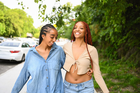 Street style portrait beautiful young African American female black couple. Braids hair, perfect white teeth smiling, sisters friends hugging walking outdoor in sunny summer day. Green park and cityの写真素材