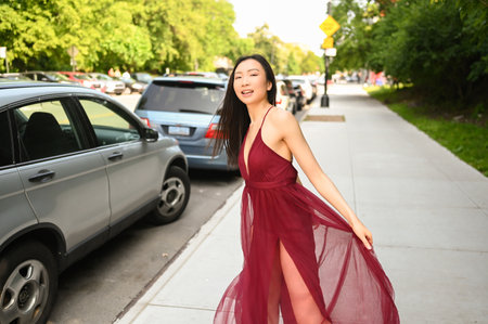 Street style outdoor portrait of Beautiful young Chinese Asian happy smiling woman walking outside sunny summer day. Attractive woman enjoys posing in front of parked cars. Big city life conceptの写真素材