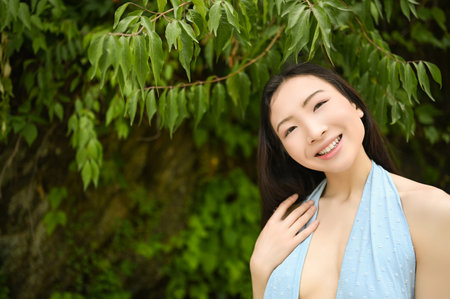 Close up outdoor portrait of Beautiful young happy Chinese Asian woman perfect skin posing outside sunny summer day green foliage. Natural facial treatment. Cosmetology, skin care and spa.の写真素材