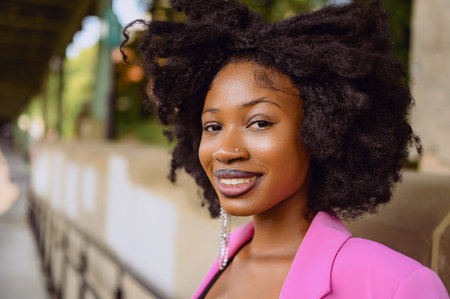 Fashion outdoor street style portrait of Beautiful young African American woman posing outside on urban city landscape summer day wearing pink jacket. Attractive black female, diversity conceptの写真素材