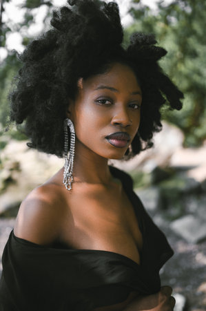 Close up headshot fashion portrait Beautiful young African American Black woman naked shoulders posing outside, sunny summer day green foliage. Facial treatment. Cosmetology, perfect skin care and spaの写真素材