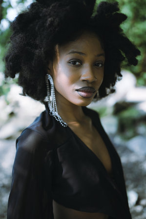 Close up headshot fashion portrait Beautiful young African American Black woman naked shoulders posing outside, sunny summer day green foliage. Facial treatment. Cosmetology, perfect skin care and spaの写真素材