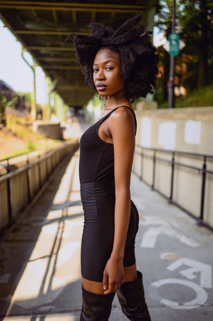 Fashion outdoor street style portrait Beautiful young African American woman posing outside on urban city landscape summer day wearing total black high leather boots.の写真素材