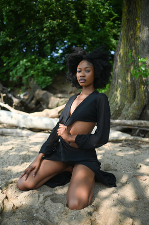 Fashion outdoor beach portrait Beautiful young African American Black woman posing outside on sandy coast with big green trees on sunny summer day. Cosmetology, natural skin body care and spaの写真素材