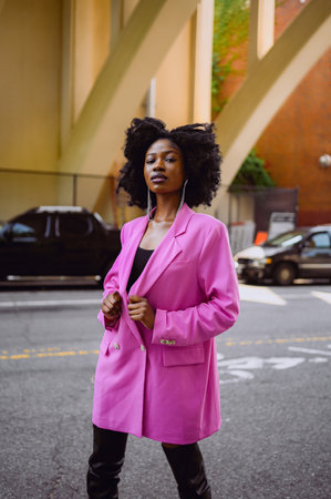 Fashion outdoor street style portrait of Beautiful young African American woman posing outside on urban city landscape summer day wearing pink jacket. Attractive black female, diversity conceptの写真素材