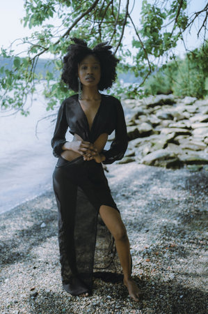 Fashion outdoor beach portrait Beautiful young African American Black woman posing outside on sandy coast with rocks and green trees on sunny summer day. Cosmetology, natural skin body care and spaの写真素材