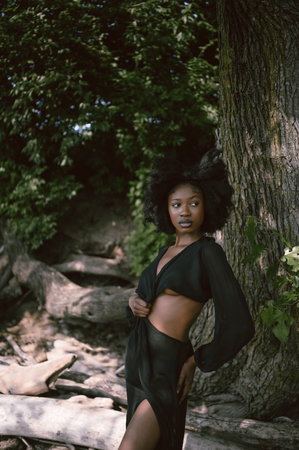 Fashion outdoor beach portrait Beautiful young African American Black woman posing outside on sandy coast with big green trees on sunny summer day. Cosmetology, natural skin body care and spaの写真素材