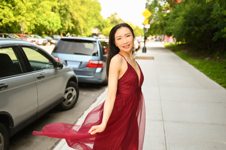 Street style outdoor portrait of Beautiful young Chinese Asian happy smiling woman walking outside sunny summer day. Attractive woman enjoys posing in front of parked cars. Big city life conceptの写真素材