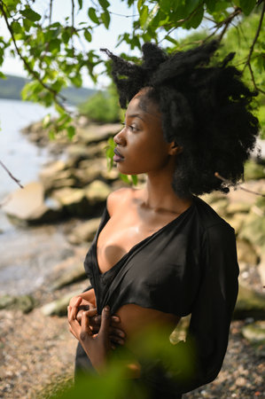 Fashion outdoor beach portrait Beautiful young African American Black woman posing outside on sandy coast with big green trees on sunny summer day. Cosmetology, natural skin body care and spaの写真素材