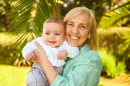 Beautiful happy smiling senior elderly woman holding on hands cute little baby boy. Grandmother and...