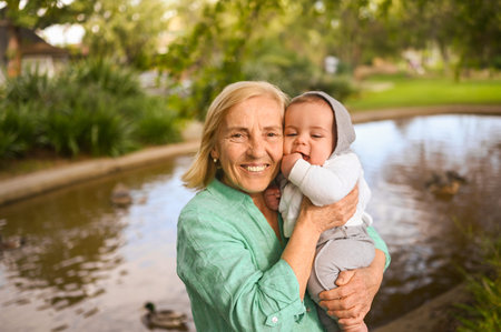 Beautiful happy smiling senior elderly woman holding on hands cute little baby boy. Grandmother and...